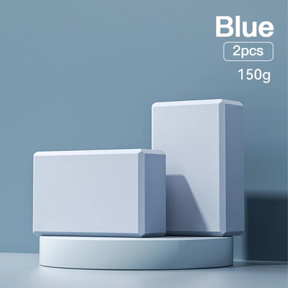 Two blue high-density foam yoga blocks on a blue display stand, indicating 'Blue, 2pcs, 150g'.